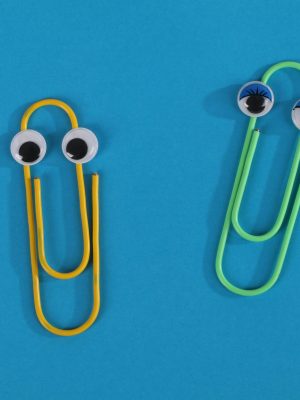 Whimsical image of yellow and green paperclips with googly eyes on a blue surface, creating a playful office theme.