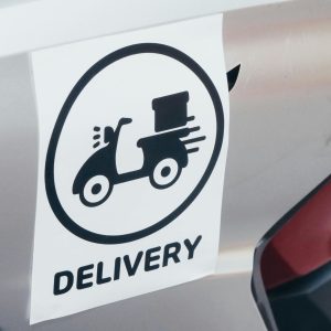 A delivery sticker featuring a scooter on a motorcycle's metallic surface.